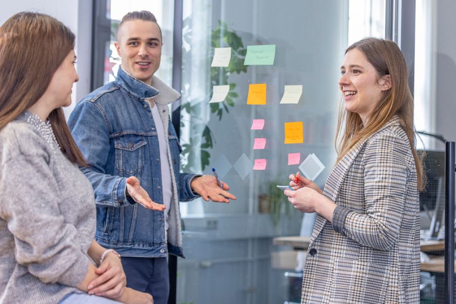 Studierende arbeiten im Team, kleben Aufkleber auf das Glas, machen ein Brainstorming, machen Notizen