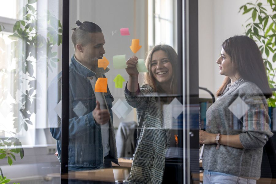 Studierende arbeiten im Team, kleben Aufkleber auf das Glas, machen ein Brainstorming, machen Notizen