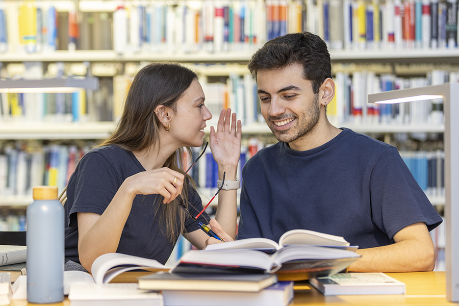 Studierende unterhalten sich und lesen Bücher in der Bibliothek